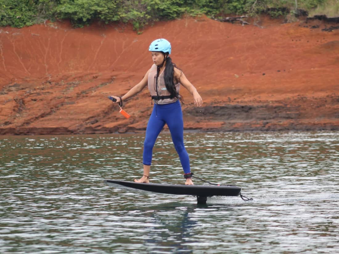 Mujer con casco y chaleco salvavidas de pie sobre el eFoil, brazos abiertos