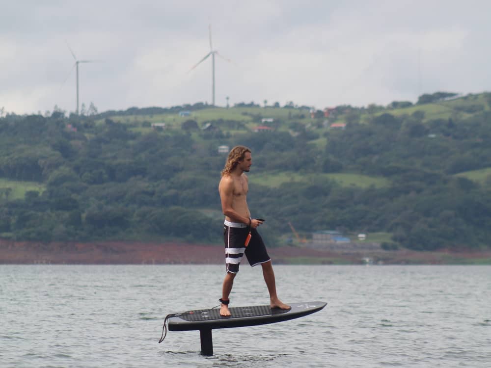 Rider volando en eFoil con las turbinas eólicas del Lago Arenal al fondo